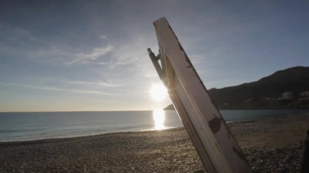 Starszy Człowiek Maluje Obraz Plaży Zbliżenie Płótno Przeciwko Podnoszeniu Słońce — Wideo stockowe