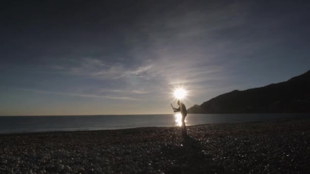 Un hombre mayor pinta un cuadro en la playa. Amplio plano de pintura masculina de edad avanzada de pie contra la elevación del sol sobre la orilla del mar y las montañas. Sol de la mañana reflejado en el tranquilo agua del mar . — Vídeos de Stock