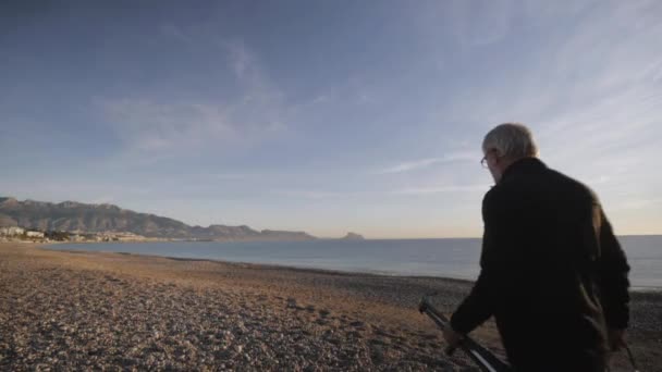Senior férfi fest egy képet a strandon. Idős férfi művész jön kavicsos tengeri strand az ő festőállvány a napfelkeltét. — Stock videók