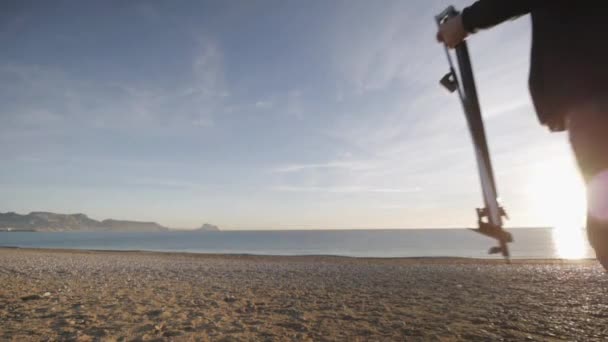 Un hombre mayor pinta un cuadro en la playa. Anciano artista masculino que llega a la playa de guijarros con su caballete al amanecer . — Vídeos de Stock