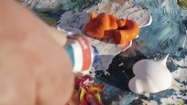 Un aîné peint un tableau sur la plage. Gros plan des mains d'artistes masculins pressant la peinture du tube sur la palette . — Video