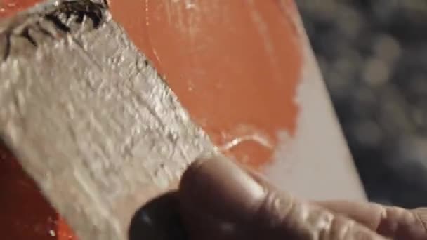 Extreme close-up shot of male artists hand painting white canvas with a wide spatula at pebble sunrise sea beach. — Stock Video