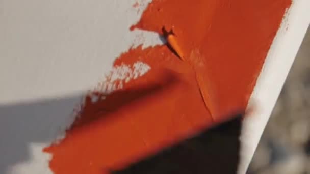 男性アーティストの手のクローズアップショットは、小石の日の出の海のビーチでキャンバスオレンジ色の塗料にへらで汚れを作ります. — ストック動画