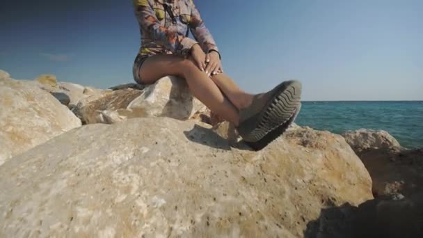 Молодая привлекательная женщина сидит на камне, глядя вдаль на закат гор и на фоне морского побережья . — стоковое видео