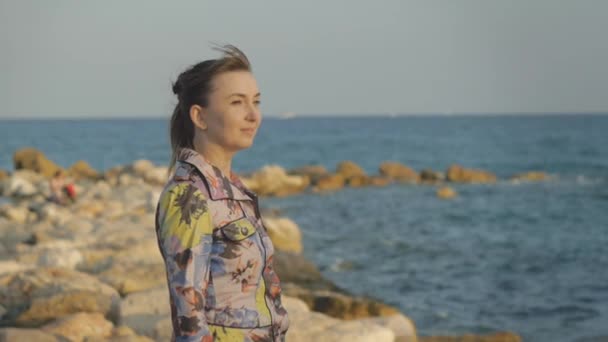 Jeune femme caucasienne attrayante souriant sur fond de côte de la mer de pierre . — Video