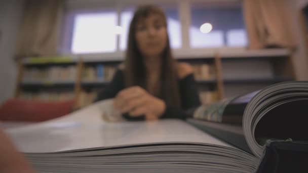 Młoda kobieta kaukaski okazuje stronę ilustrowaną książkę w bibliotece. Skupić się na książki kręgosłupa. — Wideo stockowe
