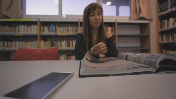 Jeune femme caucasienne tourne la page du livre illustré dans la bibliothèque . — Video