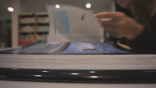 Joven mujer caucásica hojeando un libro ilustrado en la biblioteca. Disparo de ángulo bajo . — Vídeos de Stock