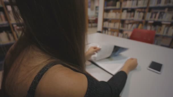 Jeune femme caucasienne feuilletant un livre illustré dans la bibliothèque . — Video