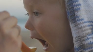 Kadın el ile örme hoodie sahil arka plan üzerine bir kaşık sarışın bebek besleme Close-up.