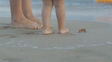 Gün batımı kumsalda oynarken beyaz genç kadın ve iki yıl eski bebek. Anne ve kızı bacaklar ayak izleri ıslak kum üzerinde bırakarak deniz kenarında duran Close-up.