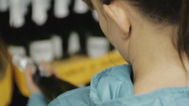 Kadın süpermarkette. Etiket üzerindeki karanlık şişe köpüklü şarap seçimi okuma mavi ceketli genç kafkas kadın Close-up.