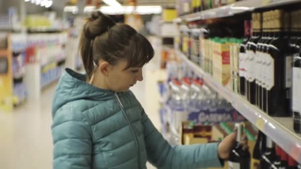 Mulher Supermercado Jovem Caucasiana Casaco Azul Lendo Rótulo Garrafa Escura — Vídeo de Stock