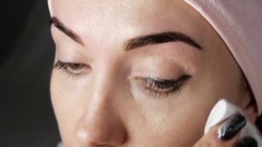 Kaşlar boyama. Kadın bir pamuk yastık ve losyon ile kaşları silerek Close-up.