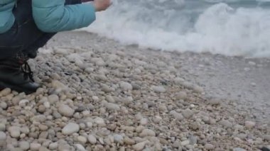 Kadın yalnız soğuk Plajı'nda. Sahilde su yakınında taşlarla oynayan çekici kafkas kadın Close-up.