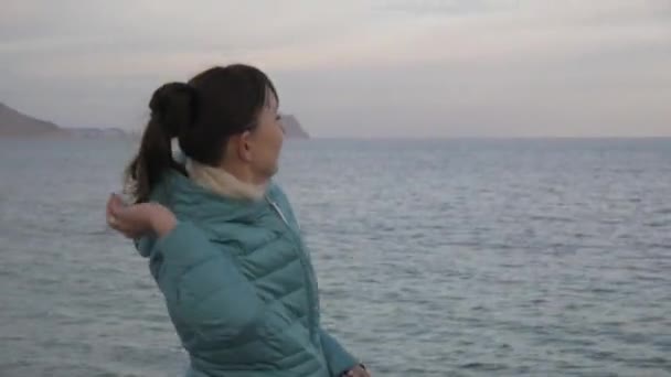 Žena v lonely beach studené. Midshot kavkazské ženy házet kameny do klidné moře. — Stock video