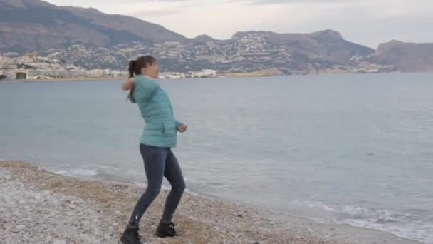 Femme à la plage froide solitaire. Femme caucasienne jette des pierres dans la mer calme . — Video