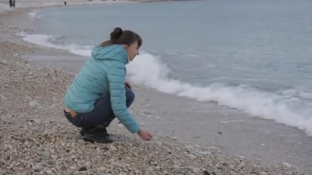 Kvinna på ensam kall beach. Attraktiv kaukasisk kvinna leker med stenar nära vattnet på stranden. — Stockvideo