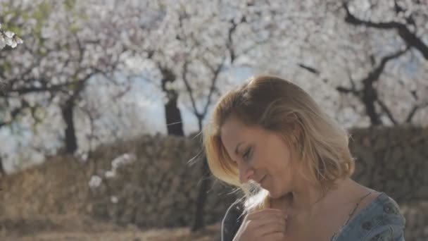 ブルーミング ガーデンの女性。アーモンドの花の木の背景に楽しい魅力的な笑顔の白人女性の肖像画. — ストック動画