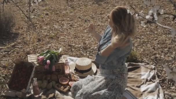 Frau im blühenden Garten. Blick von oben auf eine kaukasische Frau, die auf Schottenkarierten mit Picknick-Essen sitzt. — Stockvideo