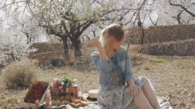 Çiçek Bahçe kadında. Saçlarını dokunmadan piknik yemekle tartan ekose üzerinde oturan çekici beyaz kadın portresi. Ağır çekim.