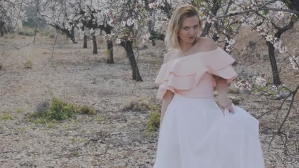 Femme dans le jardin fleuri. Plan moyen d'attrayant modèle féminin blond posant dans le parc de printemps de fleur d'amandier . — Video