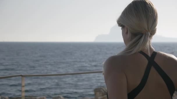 若い女性が海でポートの演習を行います。海で探しているフィットの魅力的な白人女性の背面図. — ストック動画