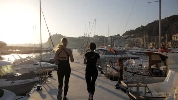 Jonge vrouwen doen oefeningen op zee haven. Fit aantrekkelijke blanke meisjes lopen langs de pier tussen de jachten. — Stockvideo