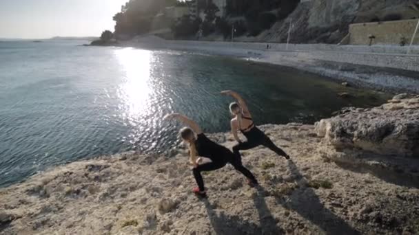 Две молодые женщины делают упражнения у моря . — стоковое видео