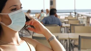 Bir kafenin terasında koruyucu maskeli genç bir kadın..