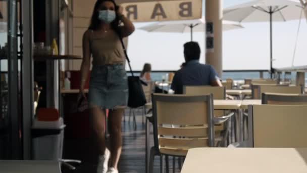 Młoda kobieta w masce ochronnej na tarasie kawiarni. — Wideo stockowe