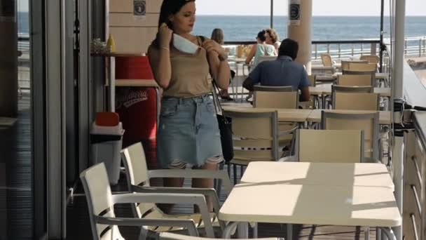 Jovem mulher em uma máscara protetora no terraço de um café. — Vídeo de Stock
