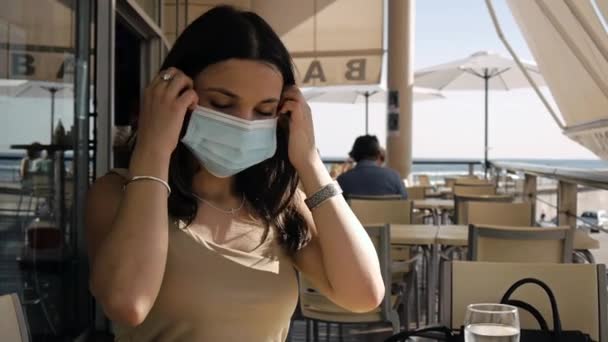 在咖啡店的阳台上戴着防护面具的年轻女子. — 图库视频影像