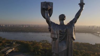 Ukrayna 'nın Kyiv kentindeki Ukrayna Anıtı' nın parkla, nehirle ve şehrin ufuk çizgisiyle çevrili kılıç ve mızrak kalkanıyla hava görüntüsü..