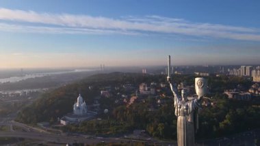 Ukrayna 'nın başkenti Kyiv' de sonbahar ağaçları, yollar ve kentsel binalarla çevrili bir kılıç ve mızrak kalkanıyla hava manzarası..