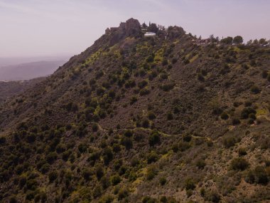 Kıbrıs 'ta engebeli bir tepenin tepesinde muhtemelen bir manastır veya kale olan tarihi yapı, seyrek bitki örtüsü ve ek binalarla çevrili bulunuyor..