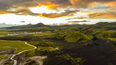İzlanda 'da tepeleri ve karanlık volkanik toprağı kaplayan yosunların hava manzarası dolambaçlı bir nehir ve gökyüzünü aydınlatan dramatik bir günbatımı..
