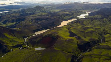 İzlanda 'nın volkanik arazisinin hava perspektifi yosun kaplı tepeler, dolambaçlı bir yansıtıcı nehir, derin vadiler ve bulutlarla kaplı dağ zirveleri içerir..