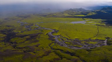 İzlanda 'nın yosunlarının hava perspektifi, örülmüş nehirler, yansıtıcı su, karanlık toprak ve sisli dağ sırtlarının yer aldığı volkanik araziyi kapsıyor..