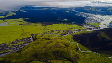 İzlanda 'nın yeşil yosunlarının hava görüntüsü tepeleri, karanlık volkanik düzlükleri ve bulutlu bir gökyüzünün altında görünen bir buzulla dönen nehirleri kaplıyordu..