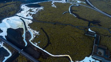 İzlanda 'da beyaz ve mavi dereleri, yosunlu lav tarlaları, modern bir yapı kompleksi ve köprüden geçen bir yol olan jeotermal arazi..