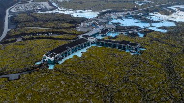 Mavi Göl jeotermal kaplıcası turkuvaz suları, modern mimari ve yeşil yosun ile İzlanda 'nın yukarısından görülen volkanik araziyi kaplamıştır..