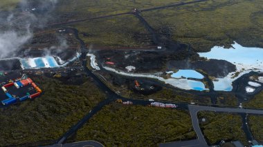 Mavi Göl 'ün sütlü mavi suları, volkanik İzlanda manzarasındaki buhar, spa tesisleri ve yollarla çevrili koyu lav sahalarıyla tezat oluşturur..