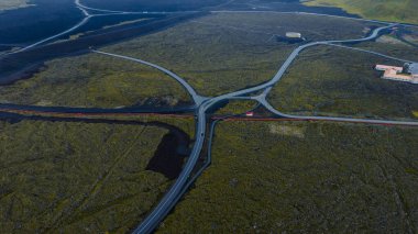 Kesişen yollar, İzlanda 'da volkanik bir arazide yosunlarla kaplı, dairesel bir yapı ve sağ üstteki bina kompleksi ile kesişiyor..
