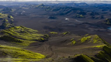 Karanlık arazi, yeşil yosun kaplı tepeler, dolambaçlı bir nehir ve engebeli dağ sırtlarının yer aldığı İzlanda 'nın volkanik dağlarının hava perspektifi.