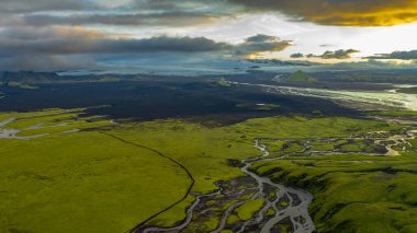 Yeşil yosun perspektifi kıvrımlı nehirlerle kaplı ovalar, volkanik bir arazi, ufukta bir buzul ve belirgin yeşil bir dağ..
