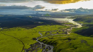 İzlanda 'nın yeşil yosunlarının hava manzarası kıvrımlı nehirlerle kaplı arazi, üçgen bir dağ, volkanik düzlükler ve gün batımında karla kaplı zirveler.