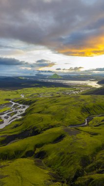 İzlanda 'nın yeşil yosunlarının hava perspektifi tepeleri, kıvrımlı nehirleri ve bulutlu gökyüzünün altında altın güneş ışığıyla birlikte üçgen bir dağı kaplıyordu..