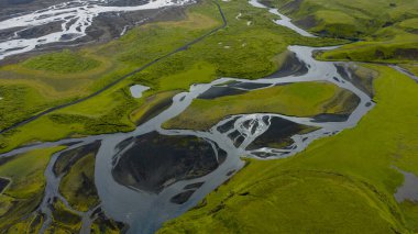 Örgülü nehir sistemi yosun kaplı arazide volkanik toprakla esiyor. İzlanda 'da yemyeşil araziyi geçen dar bir yol var..