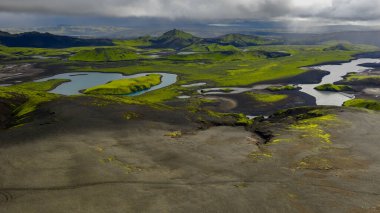 Yeşil yosun, dolambaçlı nehirler, küçük göller ve bulutlu gökyüzünün altındaki sivri dağlarla İzlanda 'nın volkanik arazisinin havadan bakış açısı.